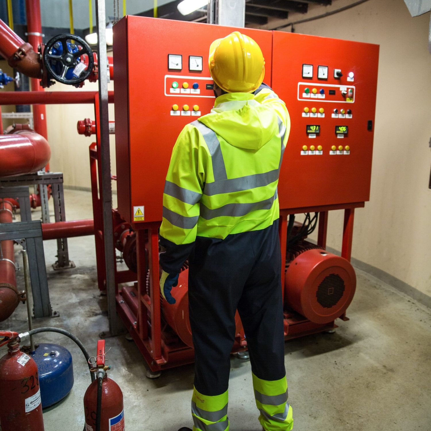 Worker in safety gear operates electrical control panel in industrial setting.